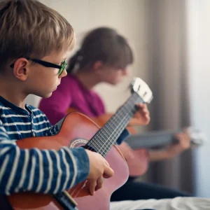 Young boy with glasses learning acoustic guitar during music lesson with instructor guidance from Legato Music