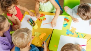 Group of young children enjoying creative art lesson with colored pencils and craft supplies at colorful tables