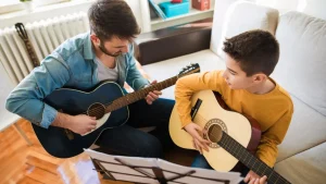 Adult guitar teacher giving individual acoustic guitar lesson to young student at home with music books from Legato Music