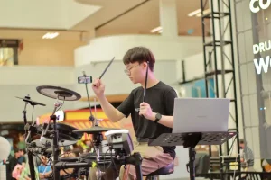Young drummer with glasses practicing electronic drums in music store with Legato Music branding in background